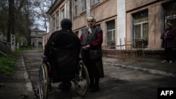 An elderly woman stands beside a man in a wheelchair outside a shelter for internally displaced people, in Dnipro, Ukraine, April 16, 2022.