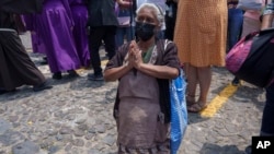 Una mujer de rodillas en oracion mientras "Cucuruchos" llevan una estatua de Jesucristo en una carroza religiosa durante una procesión del Jueves Santo, en Antigua, Guatemala, (Foto Moisés Castillo / AP)