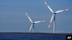 FILE - Wind turbines turn behind a solar farm in Rapshagen, Germany, Oct. 28, 2021.