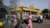 A pedestrian passes a colorful car rapide, with her image reflected in the windshield of a modern Chinese brand King Long bus. Authorities plan to phase out cars rapide by late 2018.