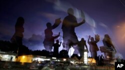 Manifestantes marchan por las calles de Ferguson iluminadas por destellos a la distancia.