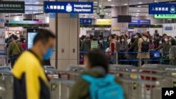 Pemudik yang memakai masker berbaris di loket imigrasi di stasiun Lok Ma Chau setelah dibukanya kembali perbatasan lintas negara dengan China daratan, di Hong Kong, Minggu, 8 Januari 2023. (Foto: AP)