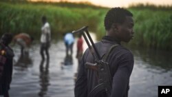 FILE - An unidentified man with a gun stands watch over displaced people, who have taken shelter from fighting, in a rebel-held part of Leer county, in Unity State, South Sudan.