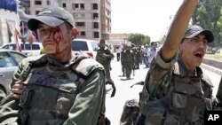 An injured Syrian army soldier (L) walks with his comrades after a roadside bomb hit their military truck, Daraa city, southern Syria, May 9, 2012. 