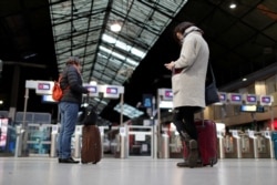 FILE - Travelers wait for a train at the Saint-Lazare railway station in Paris, Dec. 21, 2019.