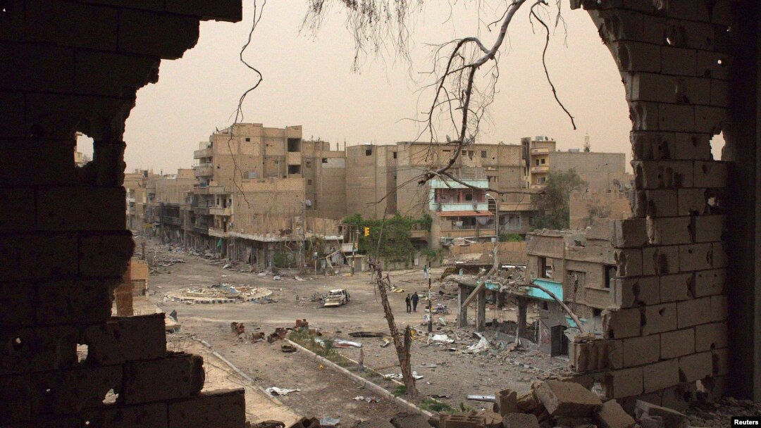 People walk down a street are pictured through a hole in a building in Deir al-Zor, Syria, April 4, 2013. 
