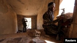 FILE - Kurdish People's Protection Units (YPG) fighters take up positions inside a damaged building in al-Vilat al-Homor neighborhood in Hasaka city, Syria.