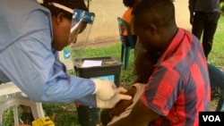 Seorang pria memeluk anak perempuannya yang berusia 5 tahun saat mendapat imunisasi vaksin Ebola yang masih dalam tahap percobaan di distrik Kasese, Uganda, 16 Juni 2019. (Foto: H. Athumani untuk VOA)