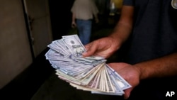 An illegal street money exchanger poses with his U.S. banknotes in downtown Tehran, Iran, Aug. 7, 2018. Money exchange shops across Iran cautiously reopened after being shut for five months.