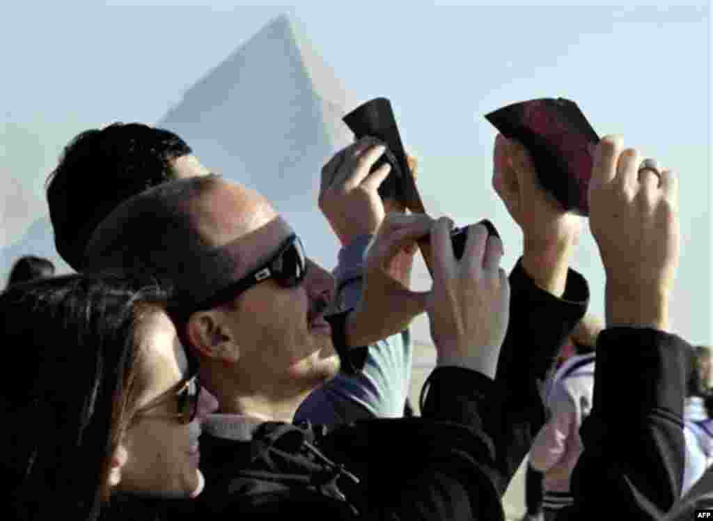 Spanish tourists watch a partial solar eclipse in front of the Giza Pyramids, Egypt, Tuesday, Jan. 4, 2011. A partial solar eclipse began Tuesday in the skies over the Mideast and will extend across much of Europe. (AP Photo/Amr Nabil)