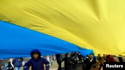 File - Children play as people hold up a giant Ukrainian flag to protest against the Russian intervention in Ukraine during the celebration of Lithuania's independence in Vilnius, Lithuania, Tuesday March 11, 2014.
