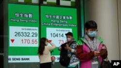 People wearing face masks to protect against the coronavirus stand in front of a bank's electronic board showing the Hong Kong share index in Hong Kong, Dec. 10, 2020.