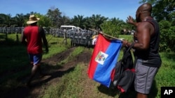 Yon migran Ayisyen kenbe drapo Ayiti pandan lap pale ak gad nasyonal Meksik pou mande yo pa arete migran ki fe pati karvann nan nan eta Chiapas, Meksik, 2 Sept. 2021. 