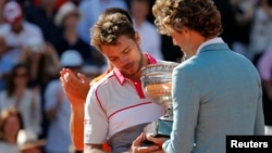 Former Brazilian tennis player Gustavo Kuerten (R) gives the trophy to Stan Wawrinka of Switzerland during the ceremony after he won the men's singles final match against Novak Djokovic of Serbia at the French Open tennis tournament, June 7, 2015. 