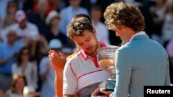 Mantan petenis asal Brazil Gustavo Kuerten (kanan) memberikan piala pada Stan Wawrinka dari Swiss di stadion Roland Garros, Paris (7/6).