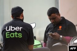 Delivery men working with the food delivery apps Uber Eats and Swiggy wait to pick up an order outside a restaurant in Mumbai, India, Feb. 6, 2019.