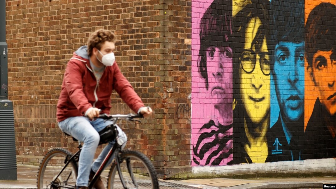 Seorang pria mengenakan masker bersepeda melewati mural band "The Beatles" di tengah pandemi virus corona, Liverpool, Inggris, 13 Oktober 2020. 