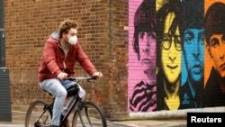 A man wearing a protective mask rides a bike past a mural depicting members of The Beatles, amid the outbreak of the coronavirus disease, in Liverpool, Britain, Oct. 13, 2020. 