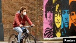 Seorang pria mengenakan masker bersepeda melewati mural band "The Beatles" di tengah pandemi virus corona, Liverpool, Inggris, 13 Oktober 2020. 