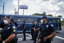 Officers stand by a City of Atlanta Corrections bus near protesters, June 13, 2020, near a restaurant where Rayshard Brooks was shot and killed by police the night before, in Atlanta, June 13, 2020.