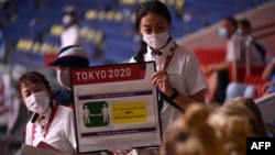 一名東京奧運會誌願者向參賽的瑞典代表隊展示新冠病毒防範措施的牌子。（2021年7月28日）
