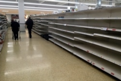 Shoppers walk past empty shelves in a supermarket in Rugby, England, March 19, 2020.