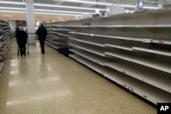 Shoppers walk past empty shelves in a supermarket in Rugby, England, March 19, 2020.