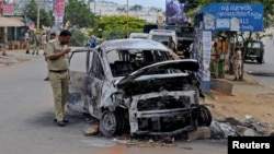 A police officer inspects the charred remains of a car set ablaze in Bangalore, following violent protests after India's Supreme Court ordered Karnataka state to release water from the Cauvery river to the neighbouring state of Tamil Nadu, India, Sept. 13