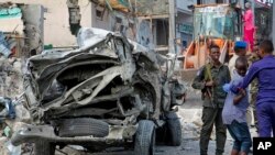 Security forces stand near the wreckage of an official vehicle that was destroyed in a bomb attack in the capital Mogadishu, Somalia Saturday, June 15, 2019. 