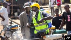 A man sprays disinfectant on a bicycle taxi in the Kibuye Market area of Kisumu, western Kenya, March 25, 2020. Riot police in the city has fired tear gas into a market Wednesday disperse crowds in hopes of limiting the spread of the coronavirus. 