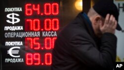 FILE - In this Dec. 16, 2014 file photo, a man walks by a sign advertising currencies of an exchange office in Moscow, Russia.