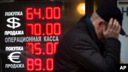 FILE - In this Dec. 16, 2014 file photo, a man walks by a sign advertising currencies of an exchange office in Moscow, Russia.