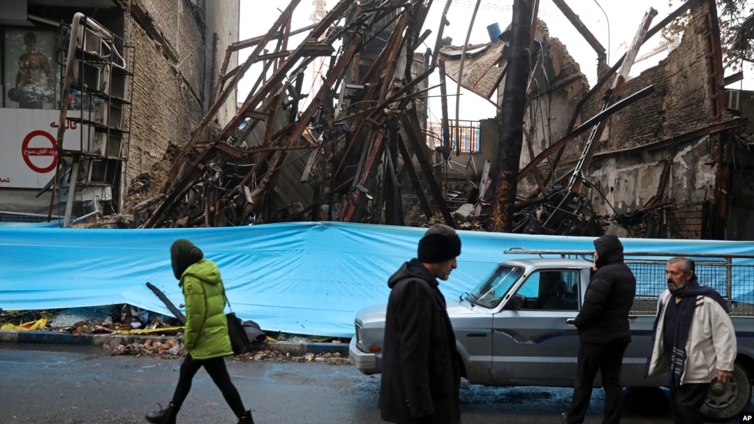 People walk past buildings that were burned during recent protests, in Shahriar, Iran, some 40 kilometers (25 miles) southwest of the capital, Tehran, Nov. 20, 2019. 