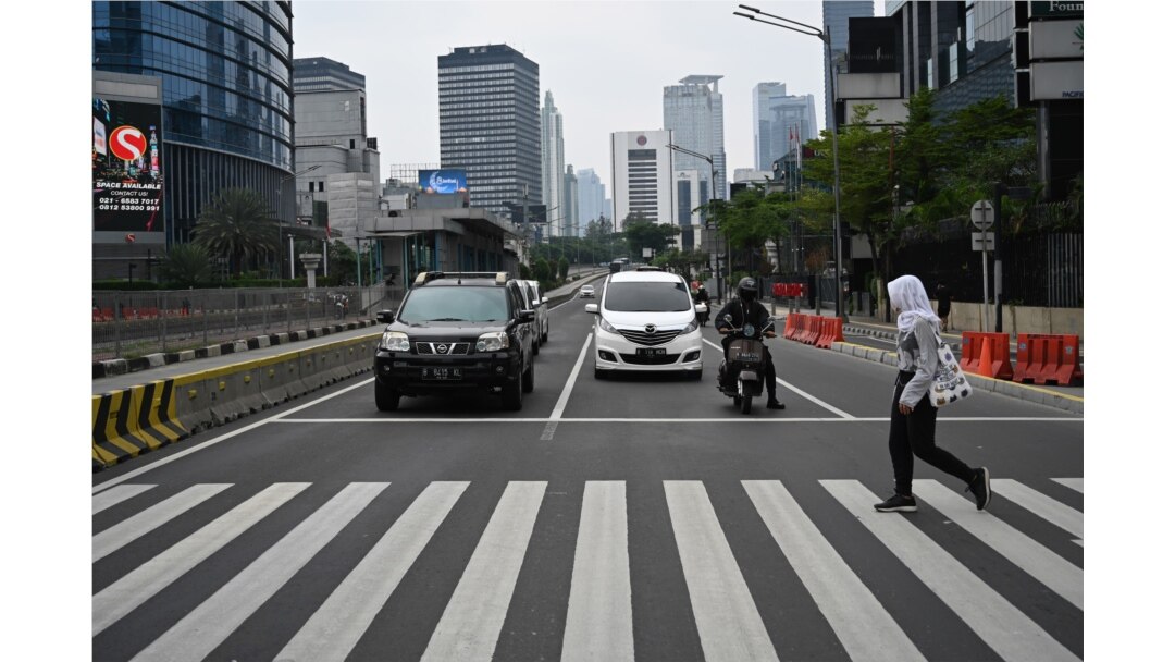 Seorang perempuan menyeberangi jalan di jalanan pusat kota Jakarta yang lengang saat diberlakukannya pembatasan di tengah pandemi Covid-19, 1 Mei 2020. (Foto oleh BAY ISMOYO / AFP)