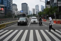 Seorang perempuan menyeberangi jalan di jalanan pusat kota Jakarta yang lengang saat diberlakukannya pembatasan di tengah pandemi Covid-19, 1 Mei 2020. (Foto oleh BAY ISMOYO / AFP)