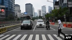 Seorang perempuan menyeberangi jalan di pusat kota Jakarta yang lengang karena PSBB di tengah pandemi corona, 1 Mei 2020. (Foto oleh BAY ISMOYO / AFP)