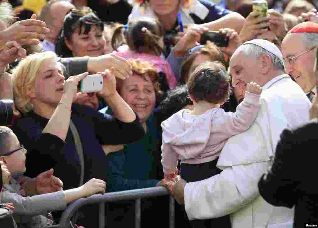 Pope Francis poses with a baby as her mother (L) takes a picture, during a visit to parish San Gregorio Magno in Rome, April 6, 2014.