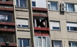 FILE - A woman stands on a a balcony during a curfew set up to help prevent the spread of coronavirus in Belgrade, Serbia, April 19, 2020.