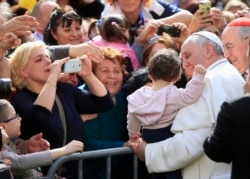 FILE - Pope Francis poses with a baby as her mother (L) takes a picture, during a visit to parish San Gregorio Magno in Rome, April 6, 2014.