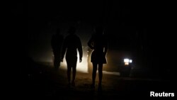 FILE: Locals are illuminated by car lights as they walk on the dark streets during frequent power outages from South African utility Eskom, caused by its aging coal-fired plants, at Lawley Township, South Africa July 13, 2022. 