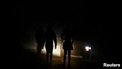 FILE - Locals are illuminated by car lights as they walk on the dark streets during frequent power outages from South African utility Eskom, caused by its aging coal-fired plants, at Lawley towship, South Africa July 13, 2022. 