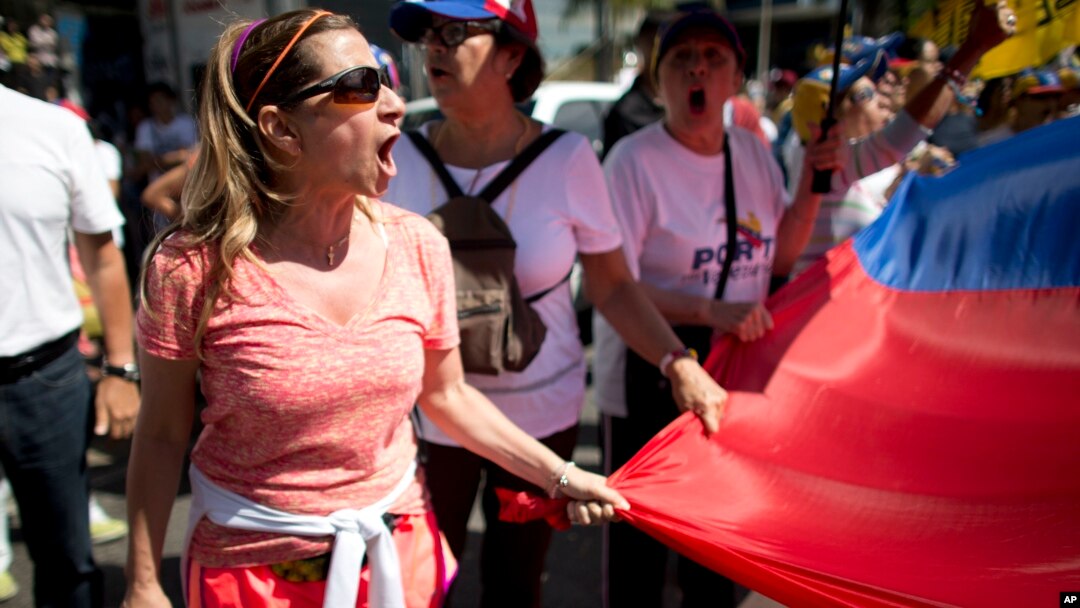 A protester chants "elections now!" as she holds the edge of a national flag, during a protest in Caracas, Venezuela, Jan. 23, 2017. 