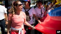 A protester chants "elections now!" as she holds the edge of a national flag, during a protest in Caracas, Venezuela, Jan. 23, 2017. 