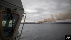 In this photo provided by the Australian Department of Defense on Jan. 6, 2020, a fire burns near Eden as HMAS Adelaide arrives to assist with wildfires.