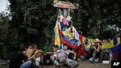 Migrantes se siente debajo de un aviso que marca la frontera entre Colombia y Panamá durante su Paso por la selva del Darién, el 9 de mayo de 2023. El presidente colombiano propuso que el levantamiento de sanciones contra Venezuela aliviaría esa crisis.