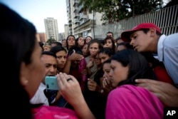 Relatives of prisoners watch in a mobile phone a video released by the prisoners outside of Venezuelan political police headquarters, SEBIN, in Caracas, Venezuela, Wednesday, May 16, 2018.