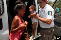 A Mexican immigration agent holds a woman's baby as she adjusts her bag so she can get into the agent's vehicle as he takes them and other Central American migrants into custody on the highway to Pijijiapan, Mexico, April 22, 2019.