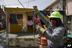 FILE - Ezequiel Rivera works with the Puerto Rico Electric Power Authority to restore distribution lines damaged by Hurricane Maria in the Cantera community of San Juan, Puerto Rico, Oct. 19, 2017.