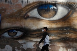 A boy wearing a face mask to help curb the spread of the coronavirus walks past a mural by British street artist My Dog Sighs, in Rome's Trastevere neighborhood, Italy, Nov. 9, 2020.