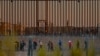 Migrants seeking asylum gather near the border wall after crossing a razor wire fence deployed to inhibit their crossing into the United States, as a member of the Texas National Guard escorts them, as seen from Ciudad Juarez, Mexico,Dec. 19, 2024. 